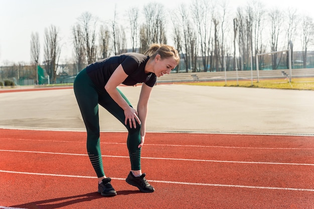 スタジアムで彼女の足を痛みで保持している若い女性。脱臼した関節のランニングスポーツ傷害骨折。