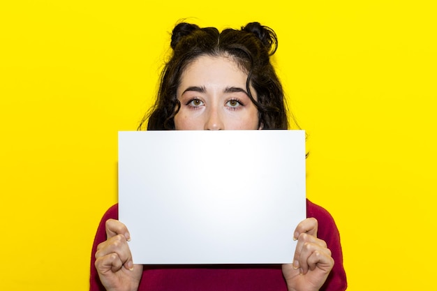 Young woman holding and hiding her face on a poster girl holding a blank poster on isolated background