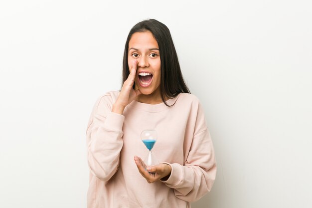 Young woman holding an hourglass shouting excited to front