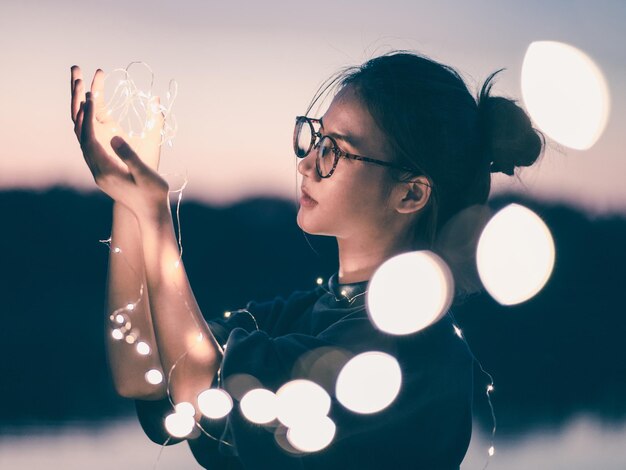 写真 照らされたストリングライトを持った若い女性