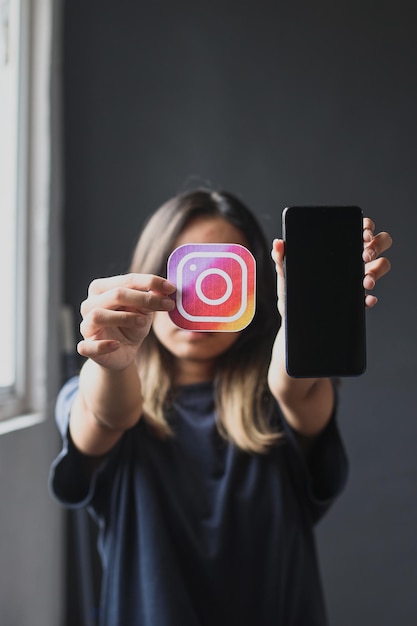 young woman holding instagram logo picture and smartphone in hands. concept of youth, technology, so
