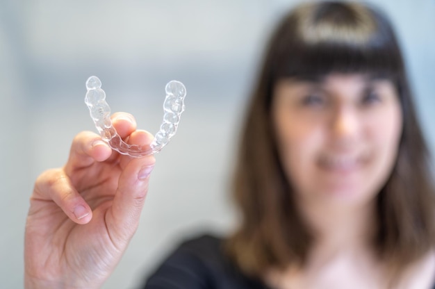 Photo young woman holding an invisible dental aligner while smiling.