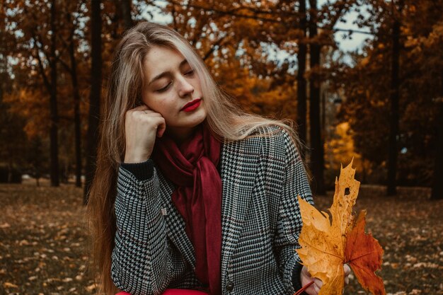 Photo young woman holding leaf while sitting against trees in forest