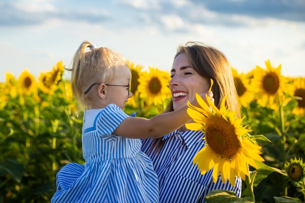 Young woman holding a little girl in her arms on a sunflower field.