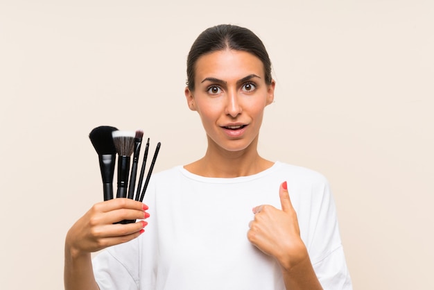 Young woman holding a lot of makeup brush with surprise facial expression
