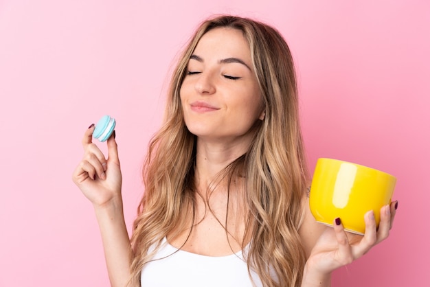 Young woman holding macarons over isolated wall