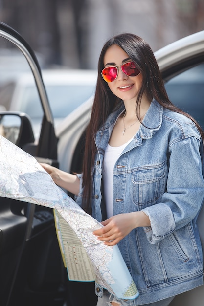 市内の地図を保持している若い女性。車の旅行に魅力的な女の子。マップ付きドライバー。