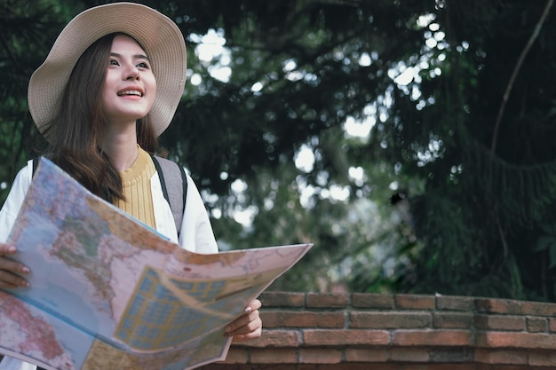 Young woman holding map looking away while standing outdoors