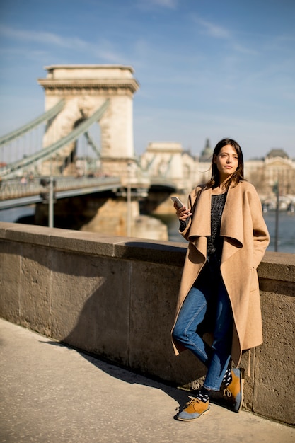 Young woman holding mobile phone with Chain bridge in background in Budapest