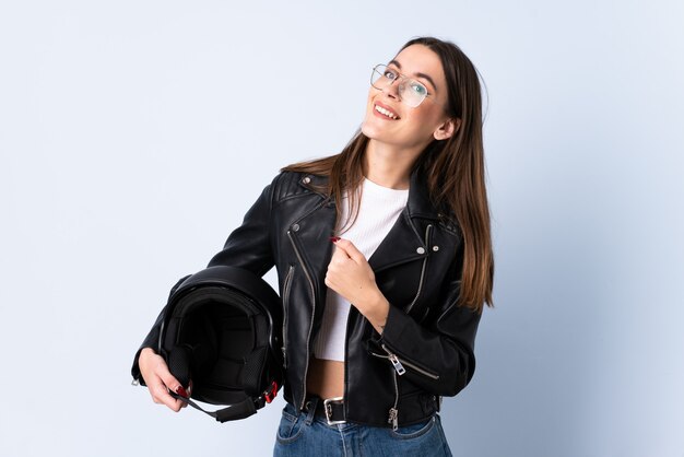 Giovane donna che tiene un casco del motociclo sopra la parete blu isolata che celebra una vittoria