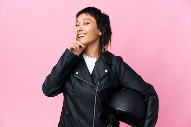 Photo young woman holding a motorcycle helmet over isolated pink doing silence gesture