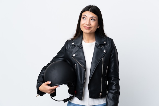 Young woman holding a motorcycle helmet over isolated white standing and looking to the side