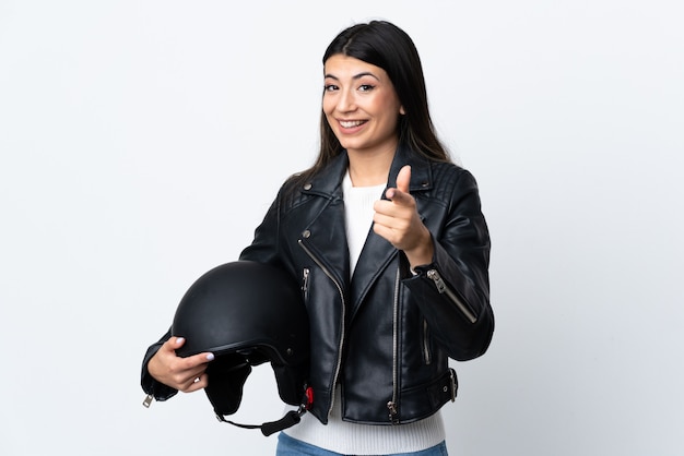당신에 고립 된 흰 벽 포인트 손가락 위에 오토바이 헬멧을 들고 젊은 여자