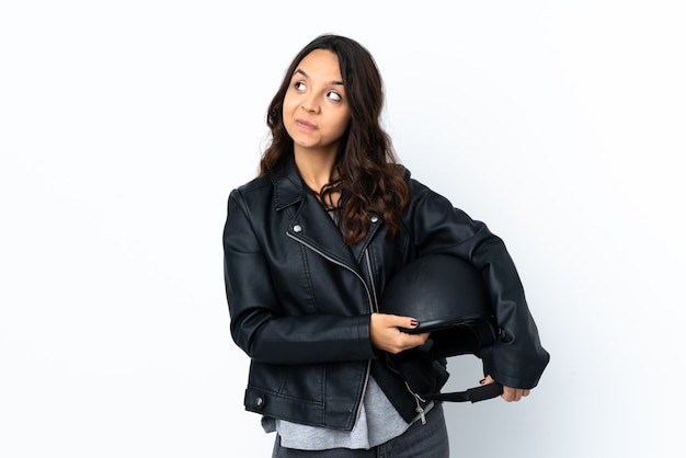 Young woman holding a motorcycle helmet over isolated white wall scheming something