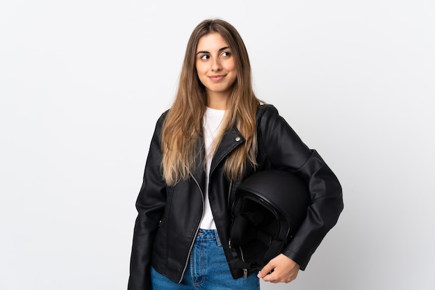 Young Woman holding a motorcycle helmet over isolated white wall standing and looking to the side