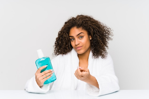 Young woman holding a mouth wash pointing with finger at you as if inviting come closer