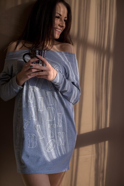 Young woman holding mug while standing against wall