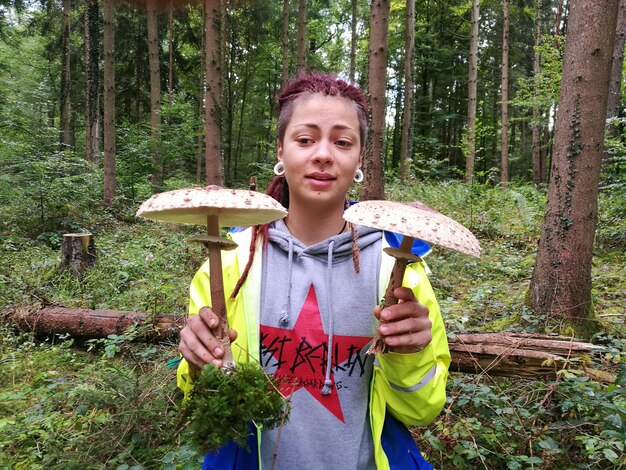 Фото Молодая женщина, держащая грибы, стоя у деревьев в лесу