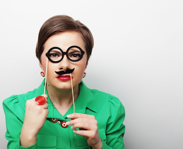 Young woman holding mustache and glasses on a stick. 