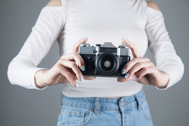 Young woman holding an old camera on a gray wall