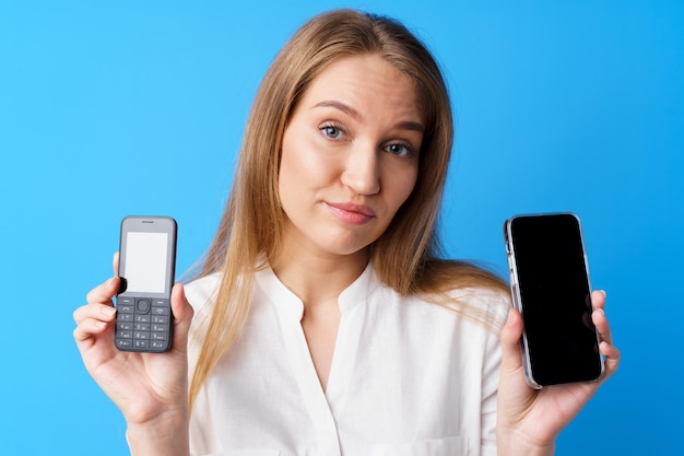 Young woman holding old and new telephone against blue background