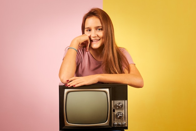 Young woman holding old retro tv sitting against yellow and pink background