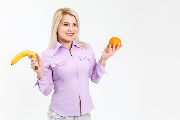 молодая женщина, держащая апельсин и банан. Изолированные над белой