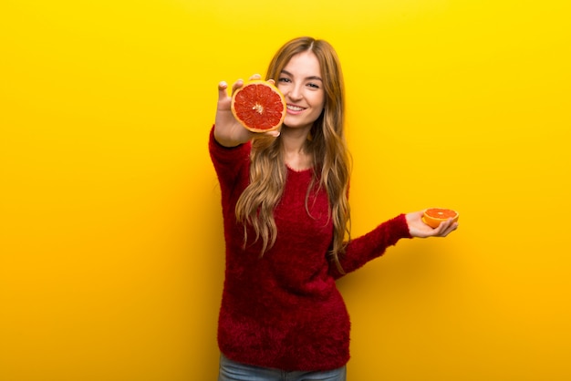 Foto giovane donna che tiene le fette arancio su vibrante su giallo