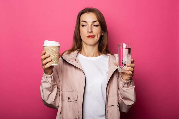 Giovane donna che tiene bicchiere di carta e bicchiere di vetro con acqua