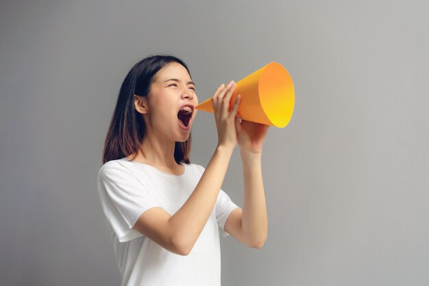 Young woman holding paper megaphone and yelling into. 