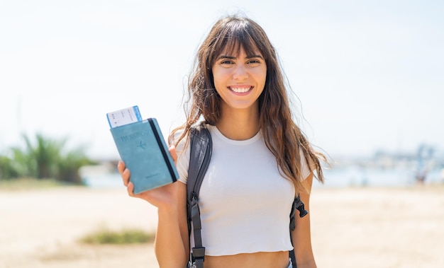 Young woman holding a passport at outdoors smiling a lot