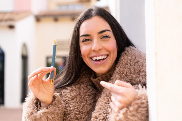 놀란 표정으로 야외에서 펜을 들고 있는 젊은 여성