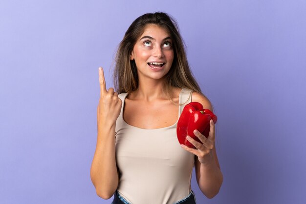 Young woman holding a pepper isolated on purple intending to realizes the solution while lifting a finger up