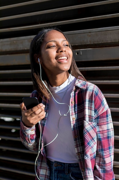 Photo young woman holding phone and singing while leaning against metallic built structure