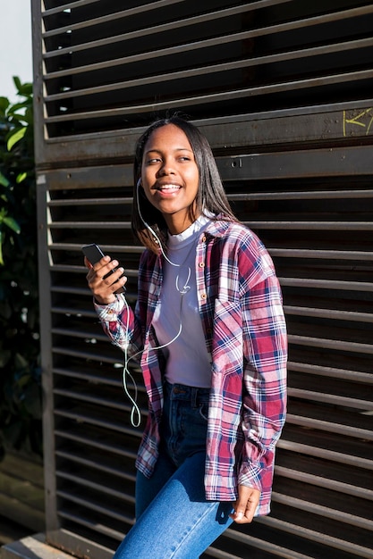 Foto giovane donna con il telefono in mano e che canta appoggiandosi a una struttura in metallo