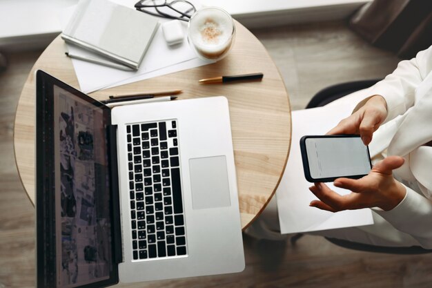 Photo young woman holding phone and working at laptop computer hands close up.  payment.  online shopping concept. working at home. quarantine and social distancing concept.