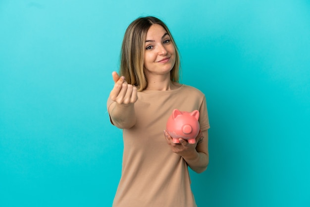 Молодая женщина, держащая копилку на изолированном синем фоне, делая денежный жест
