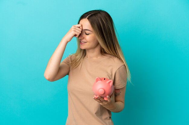 Young woman holding a piggybank over isolated blue wall laughing