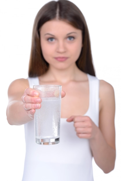 Young woman holding a pill upon glass.