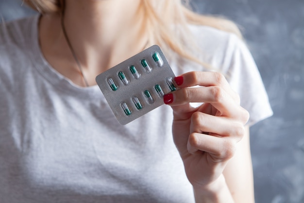 Young woman holding pills on gray