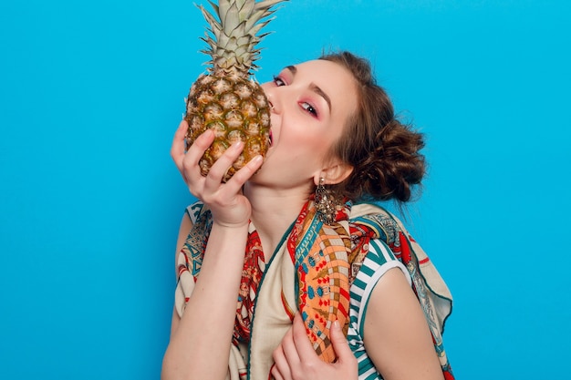 Young woman holding pineapple in hands on blue background