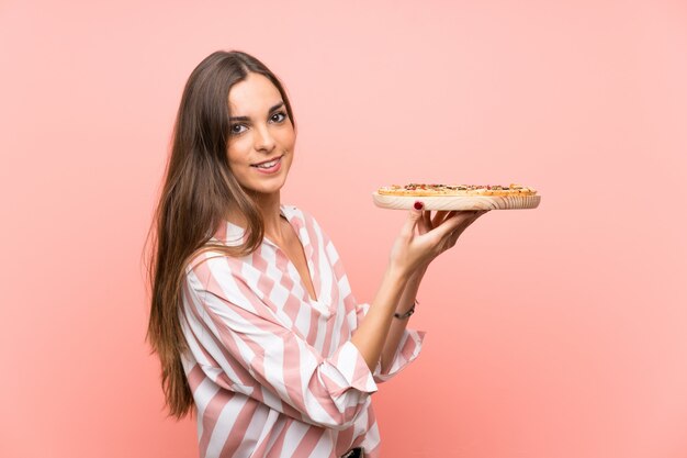 Young woman holding a pizza over isolated pink wall