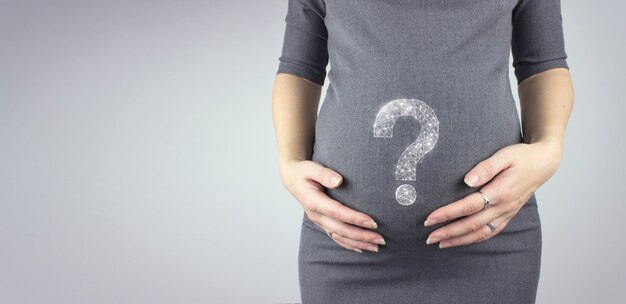 Young woman holding pregnant belly in hands with hologram question mark