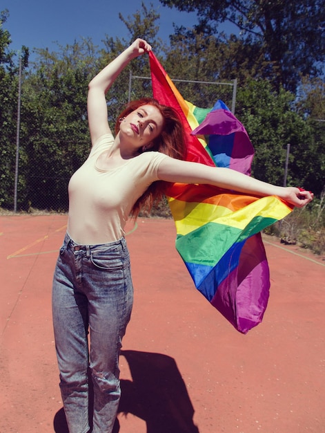 Foto giovane donna con la bandiera dell'arcobaleno sul campo da basket contro gli alberi