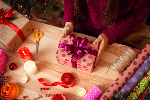 Giovane donna che tiene un regalo pronto avvolto sopra il tavolo con diverse decorazioni intorno