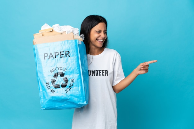 Young woman holding a recycling bag full of paper pointing finger to the side and presenting a product