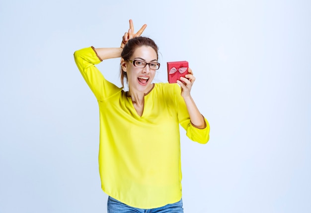 Young woman holding a red gift box and showing rabbit hear