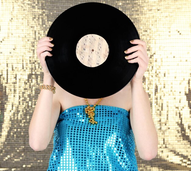 Photo young woman holding retro record in front of face on shiny background