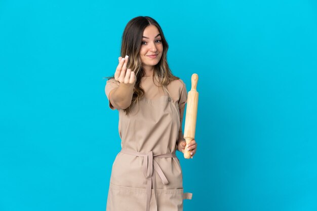 Young Woman holding a rolling pin isolated making money gesture