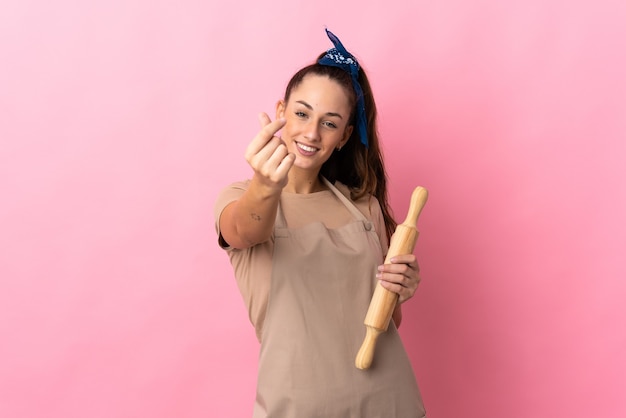 Young woman holding a rolling pin making money gesture